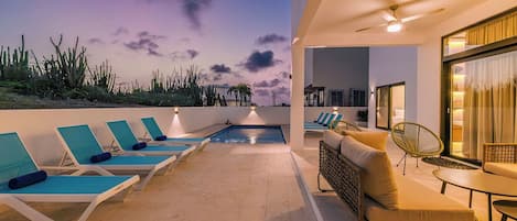 A rooftop pool area with lounge chairs and a sofa, a ceiling fan, and a view of the landscape.