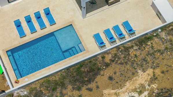 An aerial view of a swimming pool with adjacent lounge chairs and a small deck area.