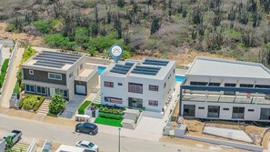 A modern multi-story residential building with solar panels, a swimming pool, and a landscaped garden.