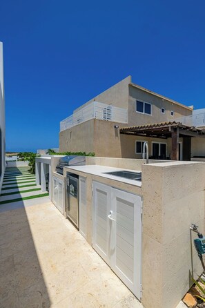 A modern house with a patio area, outdoor kitchen, and a view of the ocean.