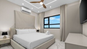 Una habitación de hotel moderna con una cama grande, un ventilador de techo, un aire acondicionado, un televisor y un ventanal con vistas.