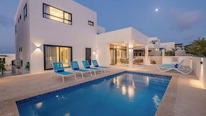 Una casa moderna de dos pisos con piscina, mobiliario exterior e ingreso bien iluminado.