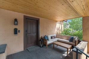 A covered outdoor seating area with a wooden bench, a sofa, and a door. - Entire Home-Charming Historic Adobe Prime Location (Santa Fe)