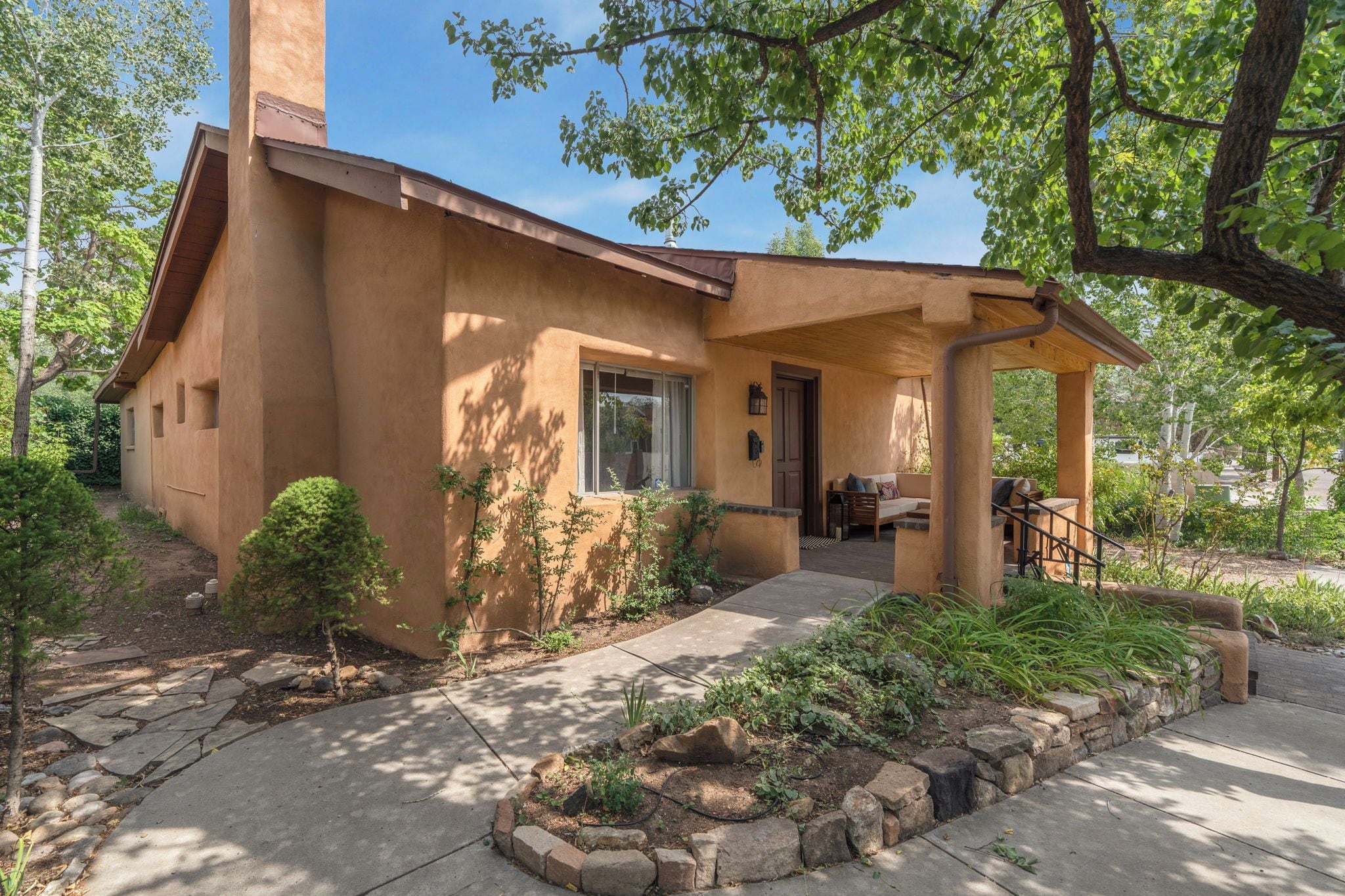 A stucco house with a covered porch, a front door, and a small garden with rocks and plants.