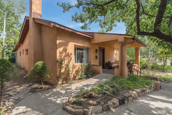 A stucco house with a covered porch, a front door, and a small garden with rocks and plants. - Entire Home-Charming Historic Adobe Prime Location (Santa Fe)
