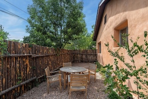 A patio with a round table and four chairs, surrounded by a wooden fence, with a building in the background. - Entire Home-Charming Historic Adobe Prime Location (Santa Fe)