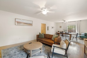 A living room with a brown sofa, a round coffee table, and a dining area with a wooden table and chairs. - Entire Home-Charming Historic Adobe Prime Location (Santa Fe)