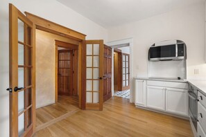 A kitchen with white cabinets, a microwave, and a wooden floor. - Entire Home-Charming Historic Adobe Prime Location (Santa Fe)