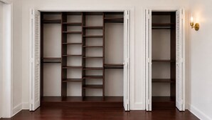 A walk-in closet with multiple shelves and hanging space, white walls, and a wooden floor.