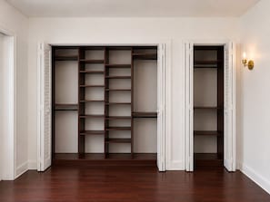 A walk-in closet with multiple shelves and hanging space, white walls, and a wooden floor.