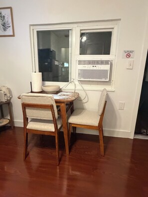 A dining area with a table, two chairs, a bowl, a roll of paper towels, and a window with an air conditioning unit. - House of VANTA on Fifteenth (Miami)
