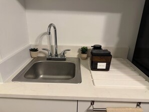 A kitchen sink with a modern faucet, a dish soap dispenser, and two small potted plants on the countertop. - House of VANTA on Fifteenth (Miami)