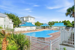 A swimming pool with lounge chairs and umbrellas, surrounded by a white fence and palm trees. - Sunnyside - 30a Blue Mountain Beach -Golf Cart or Walk to Beach With Ease (Santa Rosa Beach)