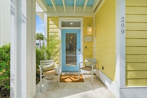 A porch with two chairs and a table, a blue door, and a sign reading 'Sunnyside Established 2009'. - Sunnyside - 30a Blue Mountain Beach -Golf Cart or Walk to Beach With Ease (Santa Rosa Beach)
