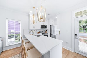 A modern kitchen with a central island, stainless steel appliances, and pendant lighting. - Sunnyside - 30a Blue Mountain Beach -Golf Cart or Walk to Beach With Ease (Santa Rosa Beach)