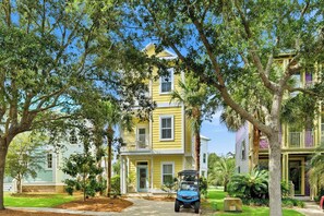 A yellow two-story house with a balcony, surrounded by trees and a golf cart parked in front. - Sunnyside - 30a Blue Mountain Beach -Golf Cart or Walk to Beach With Ease (Santa Rosa Beach)