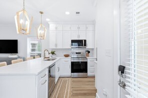 A modern kitchen with white cabinetry, stainless steel appliances, and a large island with seating. - Sunnyside - 30a Blue Mountain Beach -Golf Cart or Walk to Beach With Ease (Santa Rosa Beach)