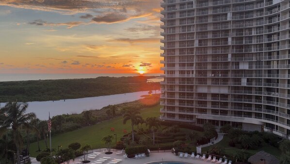 Un hotel moderno con vistas a un atardecer sobre una masa de agua, rodeado de vegetación y una zona de piscina.