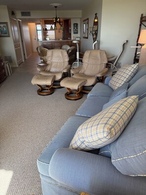 Una sala de estar con un sofá azul, sillones beige y una zona de comedor al fondo.