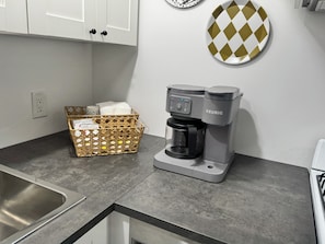 Eine Küchenzeile mit einer Kaffeemaschine, einer Serviettenkorb und einer an der Wand befestigten Platte.