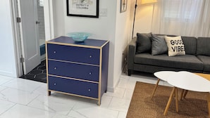 Una sala de estar con un aparador azul, un sofá gris con un cojín, una mesa blanca y una lámpara.