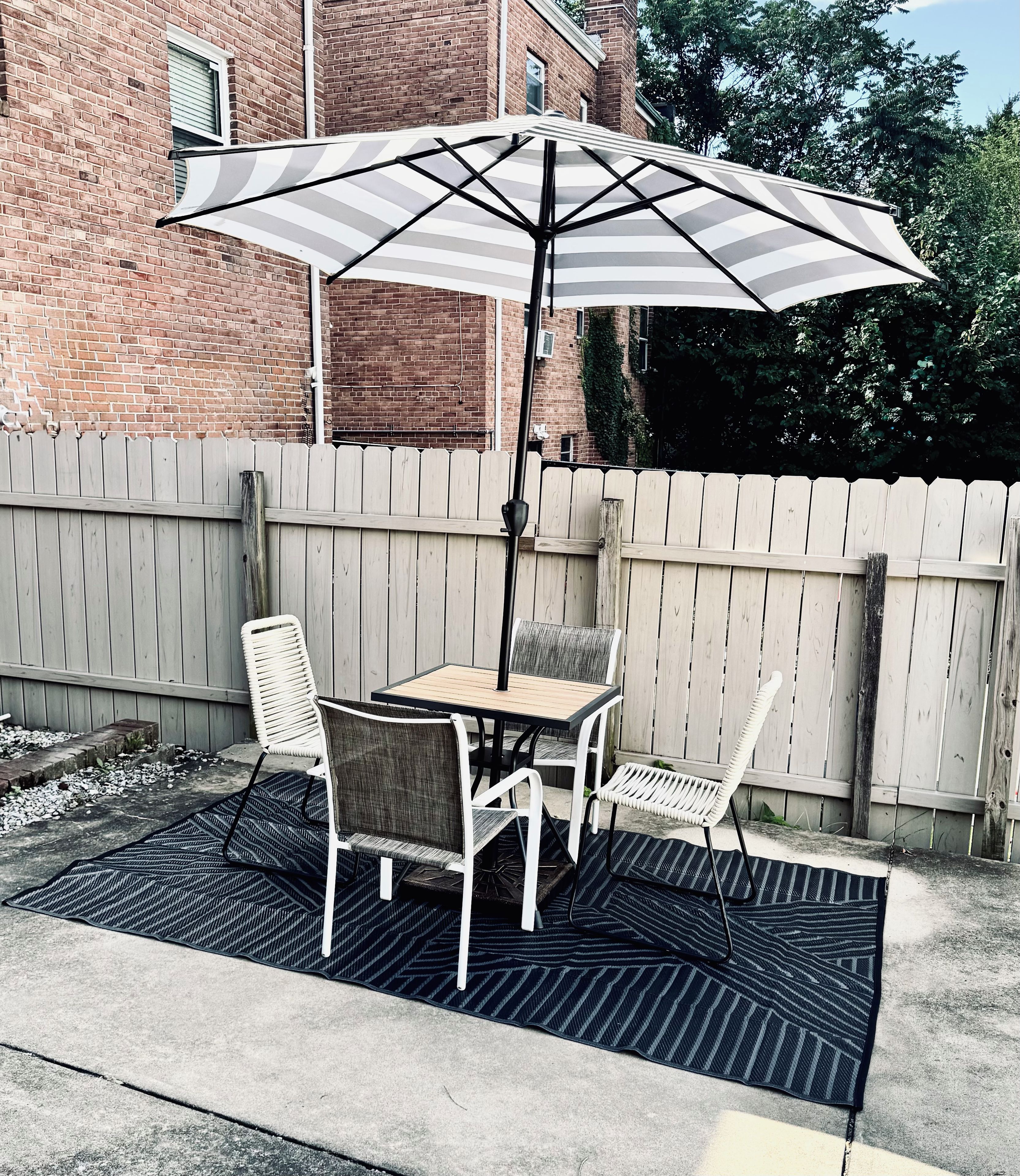 An outdoor patio with a table and chairs, a striped umbrella, and a wooden fence.