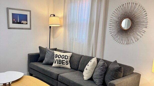 Una sala moderna con un sofá gris, una mesa redonda de centro y una mesita auxiliar.