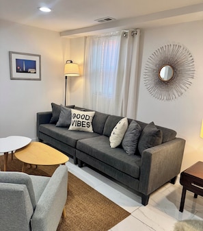 Ein modernes Wohnzimmer mit einem grauen Sofa, einem runden Couchtisch und einem kleinen Beistelltisch.