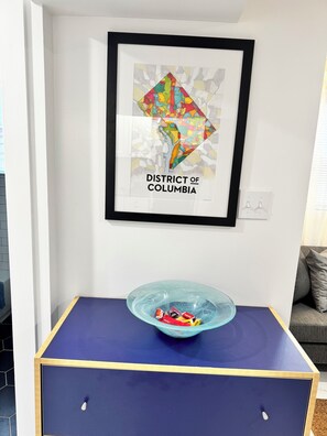 Une carte encadrée du district de Columbia accrochée au mur, un saladier en verre bleu posé sur une table et un canapé gris.
