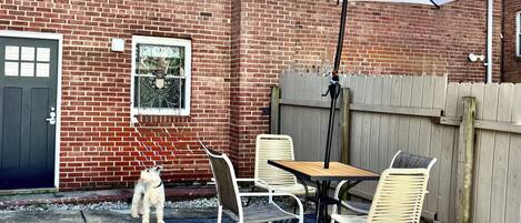 Un patio con mesa y sillas, un perro y un paraguas grande.