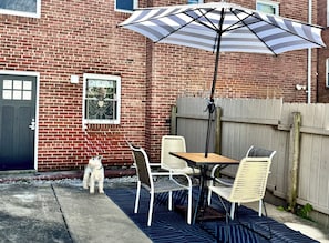 Een terras met een tafel, stoelen, een hond en een grote parasol.