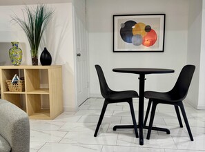 Habitació moderna amb una taula rodona i dues cadires, un armari de fusta amb cistes, i un quadre abstracte emmarcat a la paret.