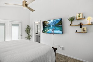 Een slaapkamer met een bed, een plafondventilator, een aan de muur bevestigde televisie en een kleine plant.