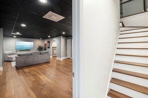 Een moderne woonkamer met een grijze bank, houten vloeren, een flatscreen televisie en een trap met houten treden.