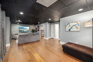 A spacious living area with a grey sofa, a brown ottoman, and a flat-screen TV mounted on the wall. - Lake Norman Private Getaway with Pool, Hot Tub & Game Room (Denver)