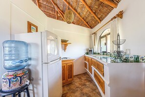 A compact kitchen with a water dispenser, a refrigerator, wooden cabinets, and a tiled backsplash. - Casita Del Mar - Steps from San Pedrito Surf Break (el Pescadero)