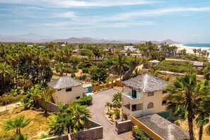 Um resort costeiro com vários edifícios no estilo de bangalô, palmeiras e vista para o oceano e montanhas ao fundo.