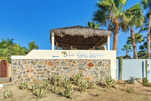 A stone wall with a sign for 'Las Palmas Tropicales Beach Front Rentals' and a thatched-roof structure. - Casita Del Mar - Steps from San Pedrito Surf Break (el Pescadero)