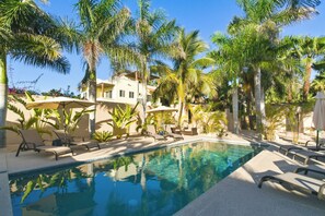 A pool area with lounge chairs and umbrellas, surrounded by palm trees and a building. - Casita Del Mar - Steps from San Pedrito Surf Break (el Pescadero)