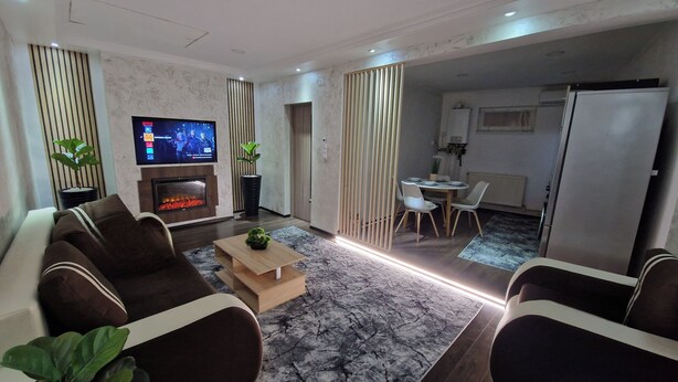 A modern living room with a flat-screen TV, a fireplace, and a dining area with a table and chairs. - Entire property with garden and free parking (Turda)