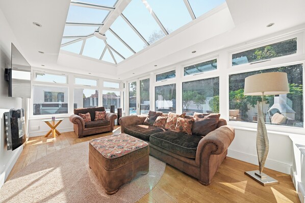 A spacious living room with a high ceiling, large windows, and a central seating area with sofas and a coffee table.