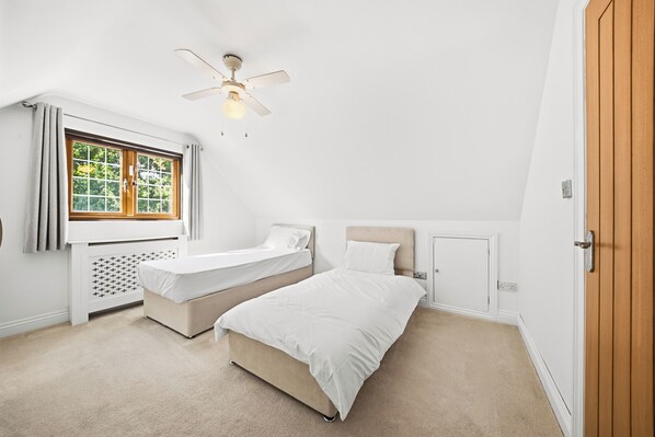 A bedroom with two beds, a ceiling fan, a window with curtains, and a door.