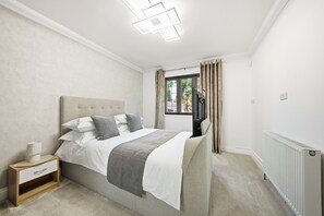 A bedroom with a bed, bedside table, lamp, window with curtains, and a radiator.