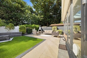 A backyard with a patio, outdoor furniture, a barbecue grill, and a well-maintained lawn.