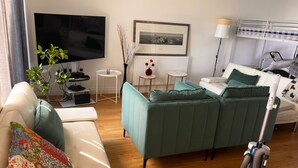 Ein modernes Wohnzimmer mit einer Couch, einem Fernseher, einem kleinen Tisch, einer Heizung und einem Staubsauger.