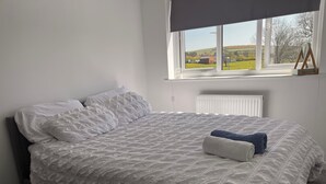 Ein ordentlich bezogenes Bett mit weißer Bettdecke und Kissen, ein Fenster mit Blick auf eine ländliche Landschaft und eine Heizung unter dem Fenster.