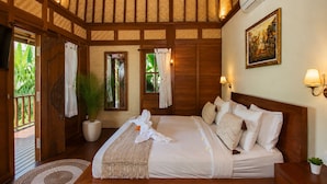 A bedroom with a large bed, wooden beams, a potted plant, and a painting on the wall. - Ubud 1BR Villa Wooden Resort Sahadewa (Gianyar)
