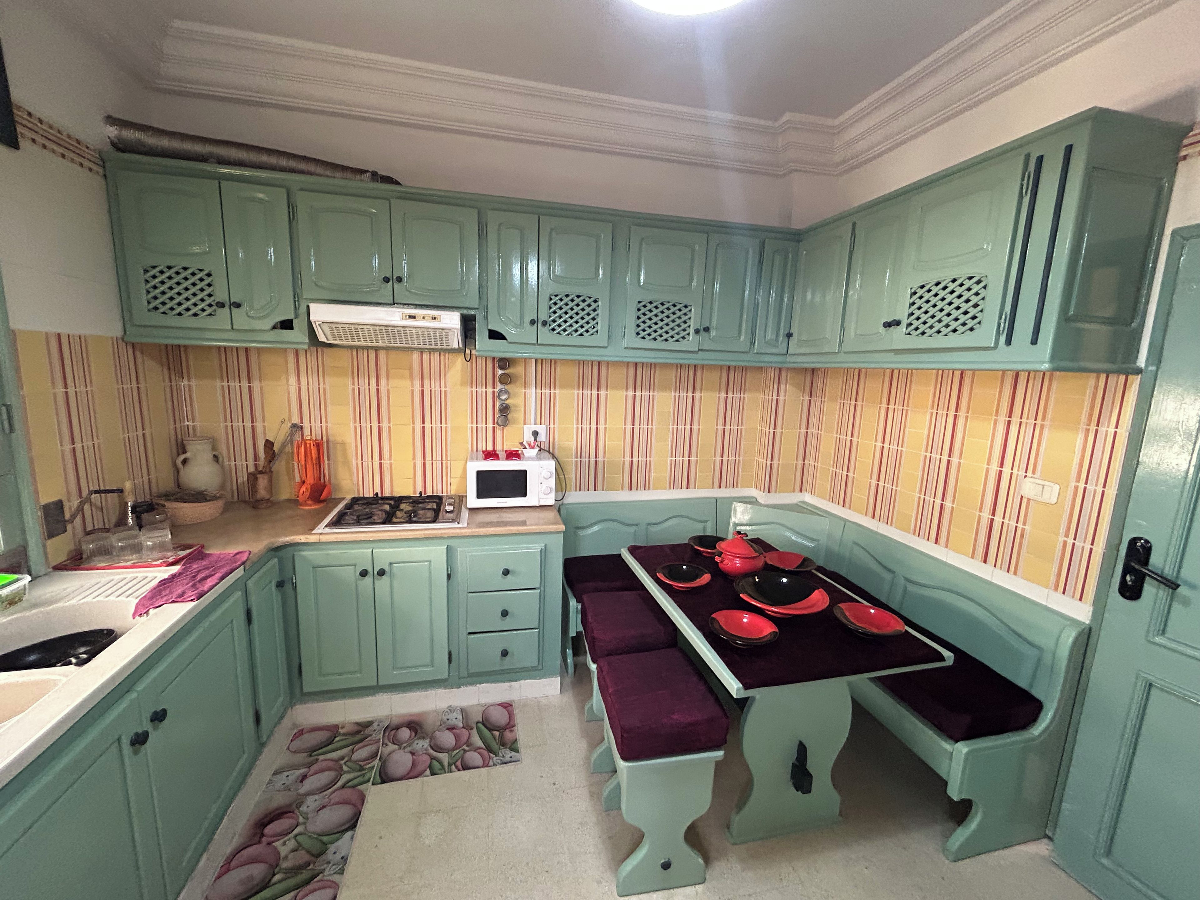 Une cuisine avec des armoires de couleur turquoise, un four à micro-ondes, une cuisinière et une table à manger avec des assiettes rouges.
