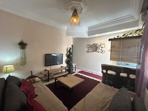 A living room with a flat-screen TV, a wooden coffee table, a sofa, a red rug, a hanging plant, and a decorative mirror. - THE MEDINA Rooftop
it’s a spacious villa in the peaceful heights of Montfleury (Tunis)