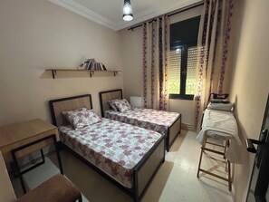Ein Schlafzimmer mit zwei Einzelbetten, einem Nachttisch, einem Sessel, einem Heizkörper und einem Fenster mit Vorhängen.